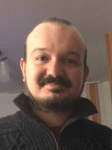 Ion Cosma Fulga mit dunklem Pulli und Bart, in Innenraumumgebung.